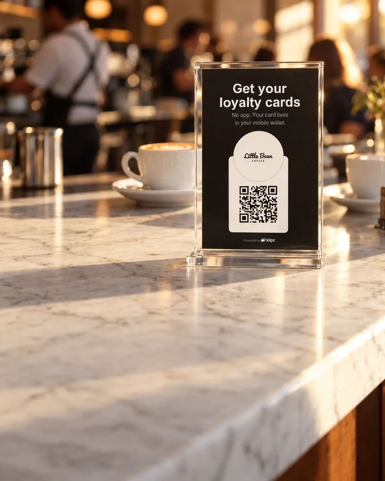 A clear stand on a marble café counter holds a black sign: "Get your loyalty cards", with Little Bean's logo over a QR code.