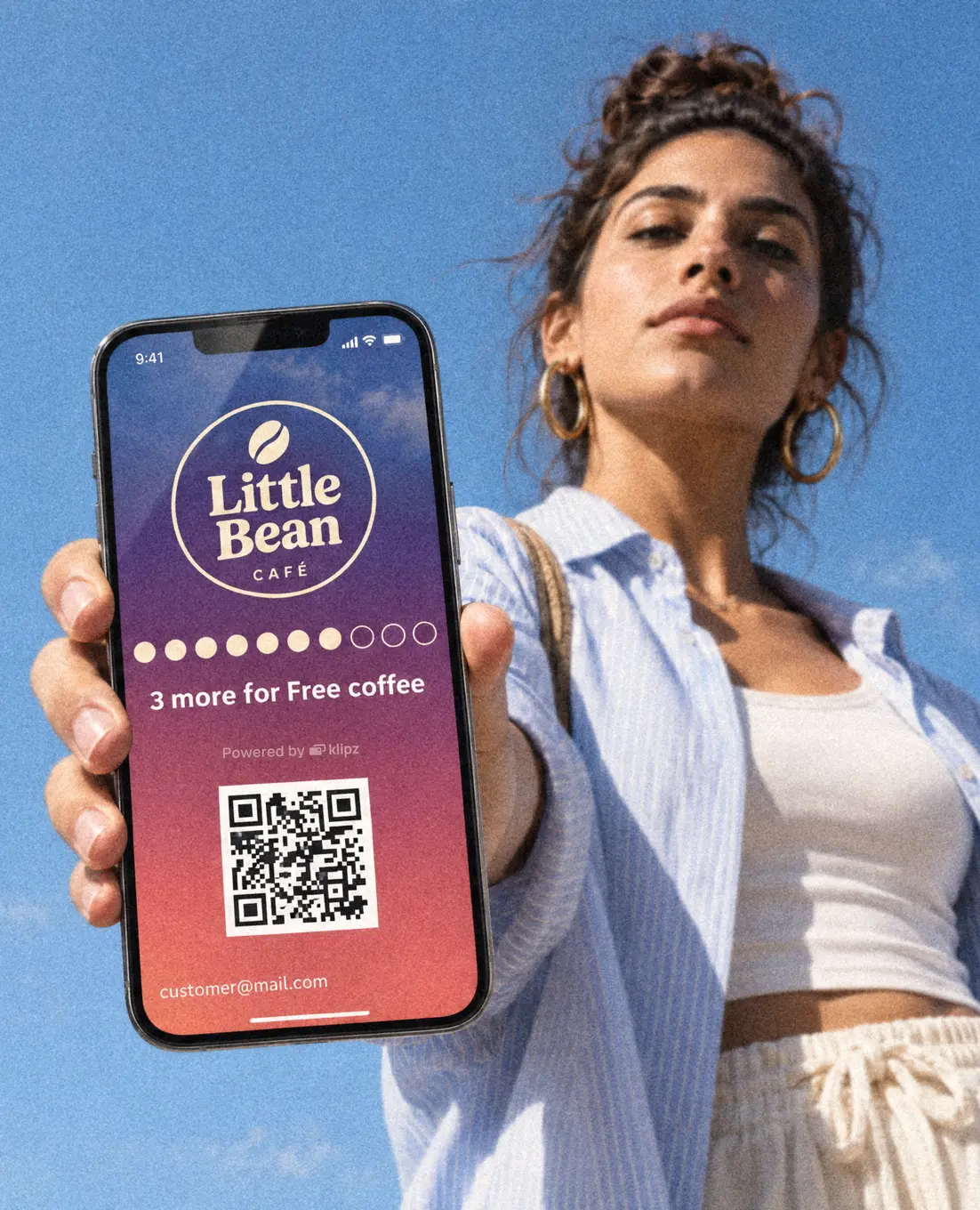 En kvinde under en blå himmel holder telefonen frem med sit medlemskab hos Little Bean åbent på skærmen.